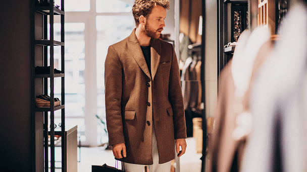 Mann probiert einen braunen Wollmantel in einer Modeboutique an