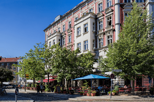 Sanierter Altbau mit Straßencafé unter Bäumen an einem Platz