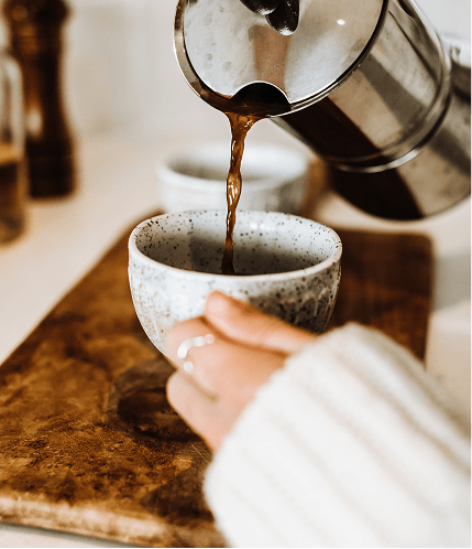 Kaffee wird aus einer French Press in eine Keramiktasse gegossen