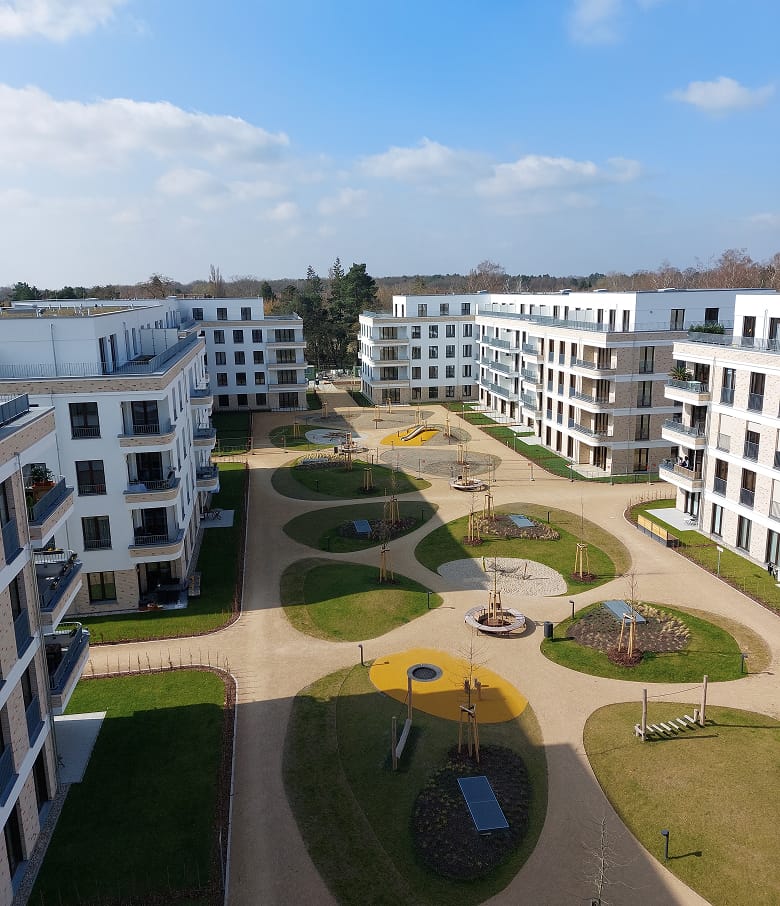 Luftaufnahme eines Wohnquartiers mit weißen Gebäuden, Grünflächen und Spielplatz im Innenhof