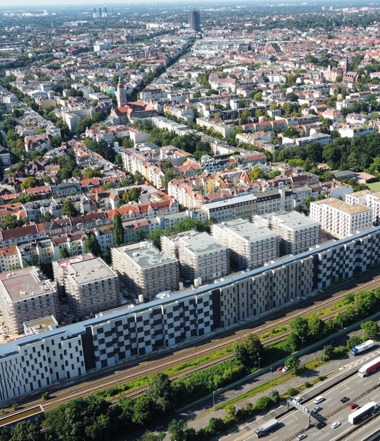 Luftaufnahme eines großen Wohnkomplexes mit Schachbrettfassade an einer Bahntrasse