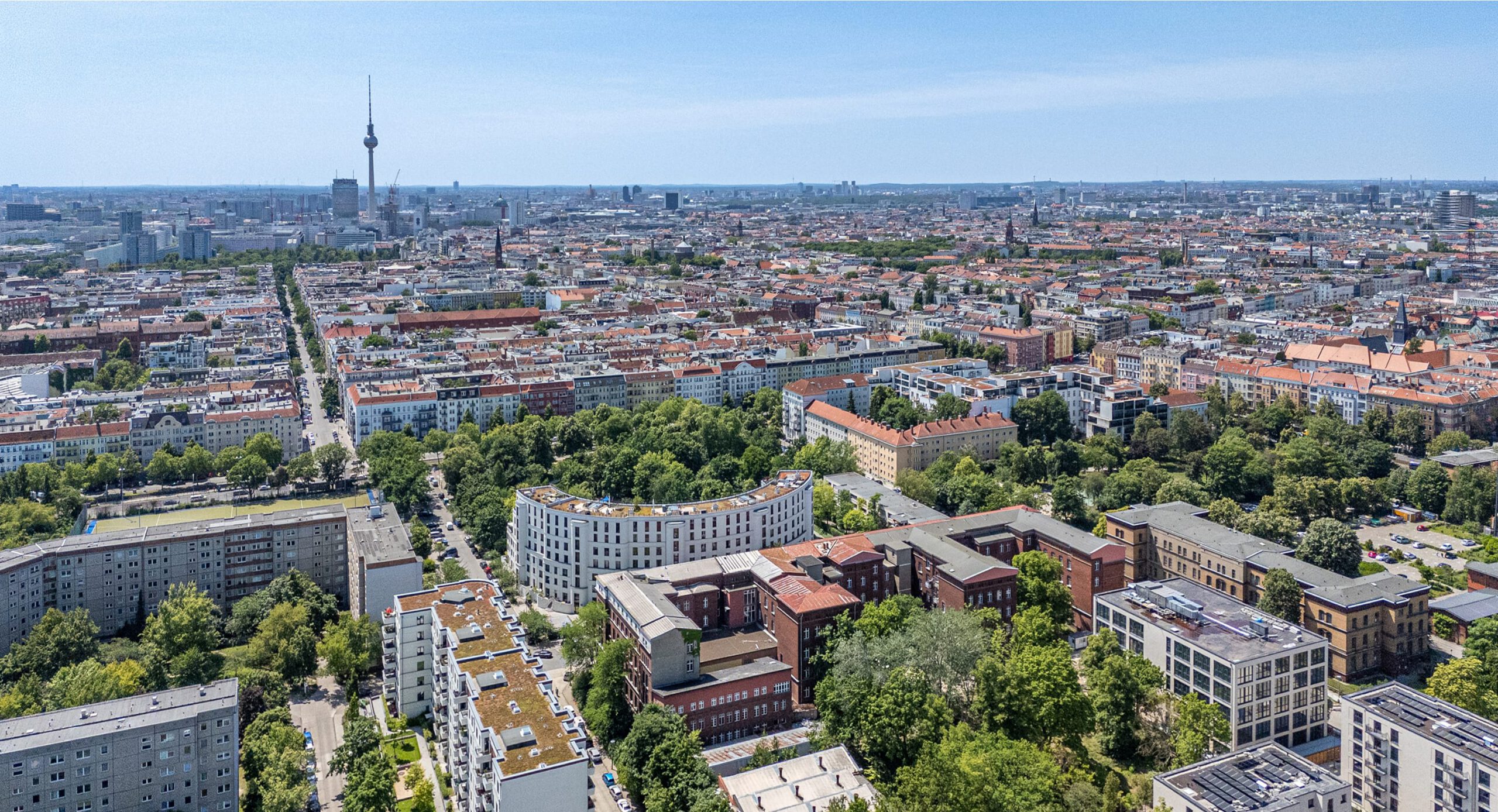 Luftaufnahme über Berliner Dächer mit Fernsehturm am Horizont und begrünten Neubauten