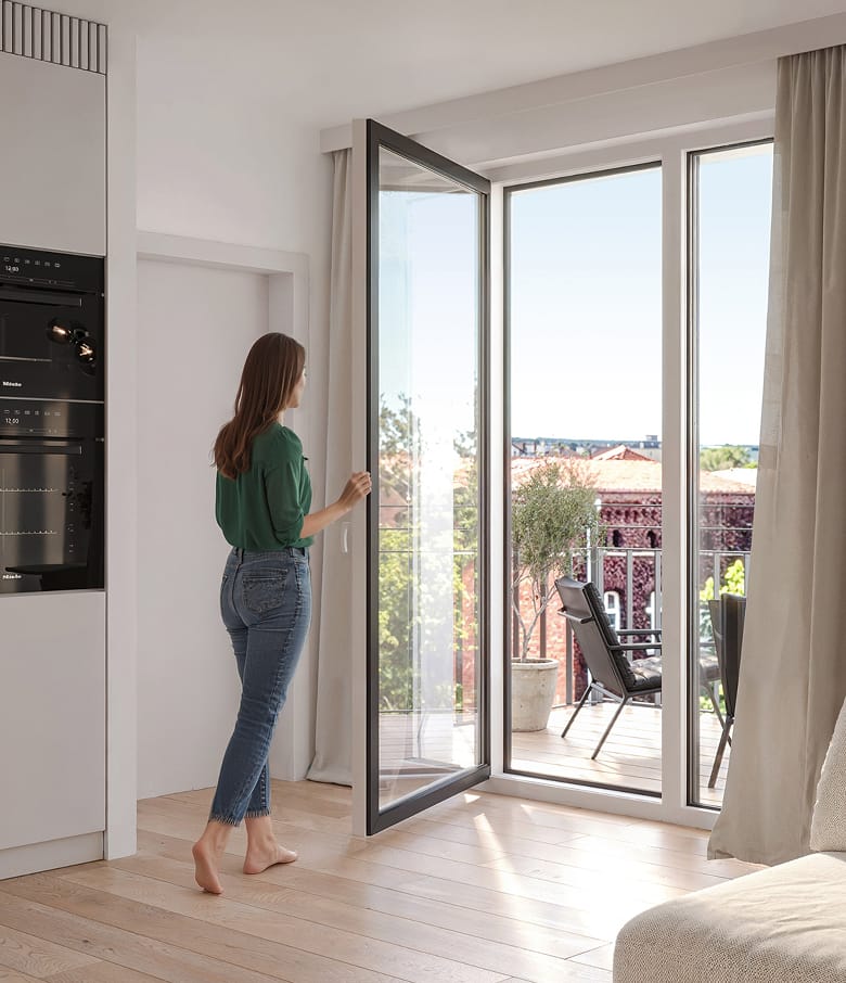 Fassade des Ella Living mit gestaffelten Balkonen und Terrassen zwischen jungen Baeumen