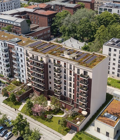 Schräge Luftaufnahme des Gebäudes mit begrüntem Solardach und blühendem Innenhofgarten