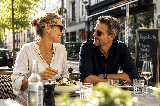 Paar genießt Wein und Essen auf einer sonnigen Restaurantterrasse im Freien