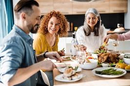 Drei lachende Menschen beim gemeinsamen Essen an einem gedeckten Tisch