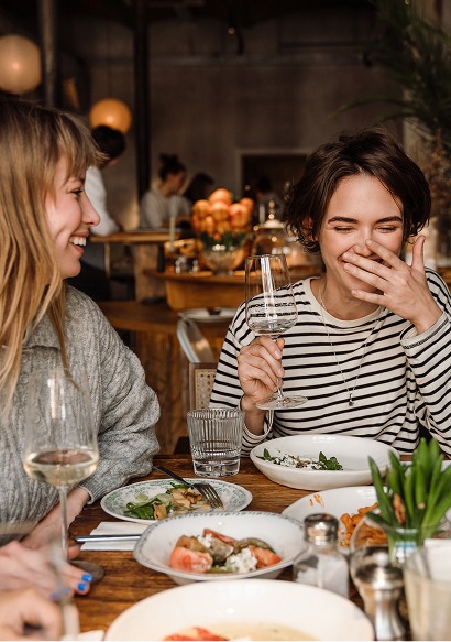 Zwei junge Frauen lachen bei Wein und Speisen an einem gedeckten Restauranttisch