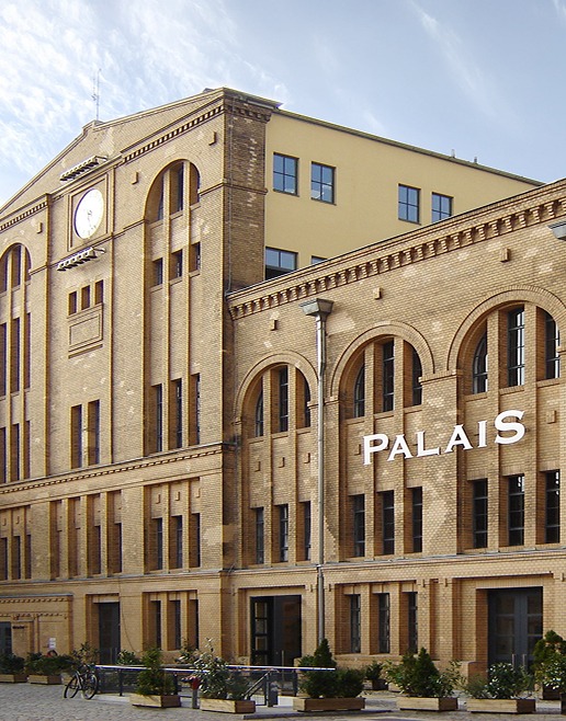 Historisches Backsteingebäude mit Uhr und Schriftzug Palais unter blauem Himmel