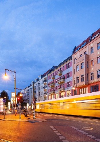 Gelbe Straßenbahn fährt zur blauen Stunde an beleuchteten Altbaufassaden vorbei