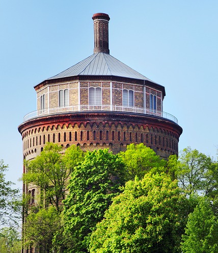 Runder historischer Backstein-Wasserturm ragt über dichte grüne Baumkronen
