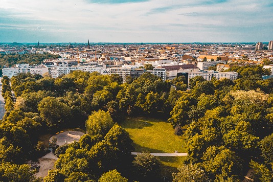 Luftaufnahme eines grünen Stadtparks mit weiter Wiese vor der Berliner Häuserkulisse